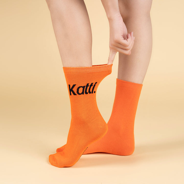 Person wearing orange socks with 'Kattie' branding on a beige background