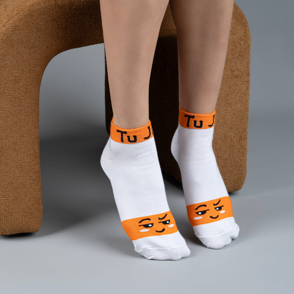 White socks with orange bands and face designs worn by a person sitting on a brown chair.