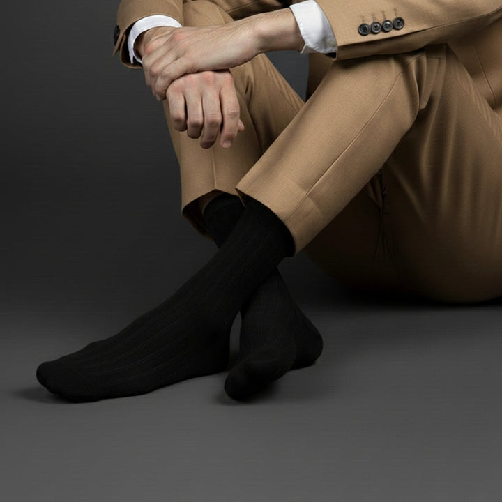 Person wearing a beige suit and black socks on a dark background