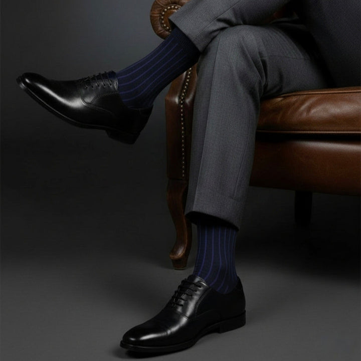 Person wearing dark gray suit and black shoes with striped socks sitting on a brown leather chair.