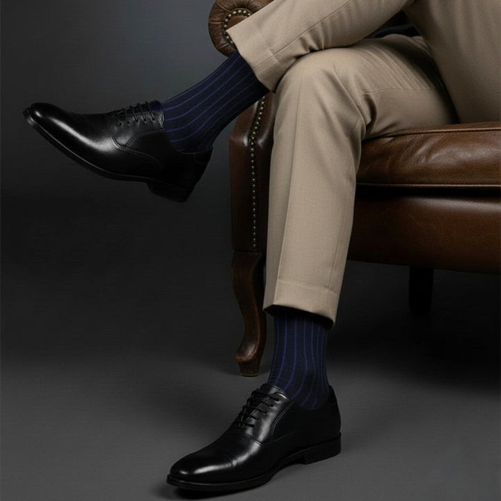 Person wearing black shoes, beige pants, and blue striped socks sitting on a brown leather chair.